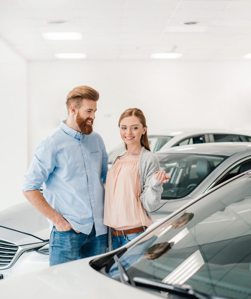 happy-couple-choosing-car-in-dealership-salon-woman-pointing-on-car-e1616394658847.jpg